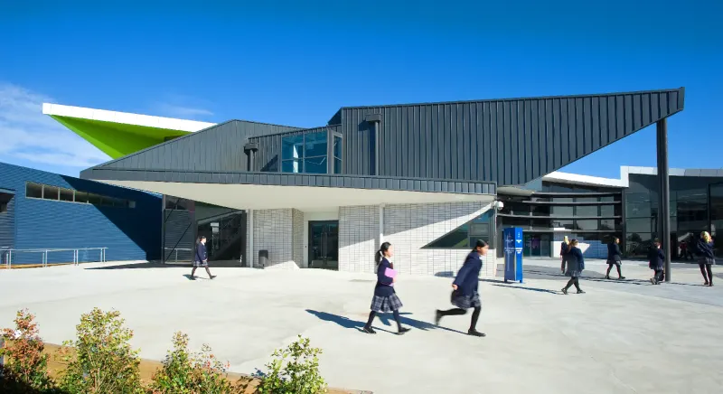 Angular secondary school entrance with green cantilevered canopy and students crossing the forecourt