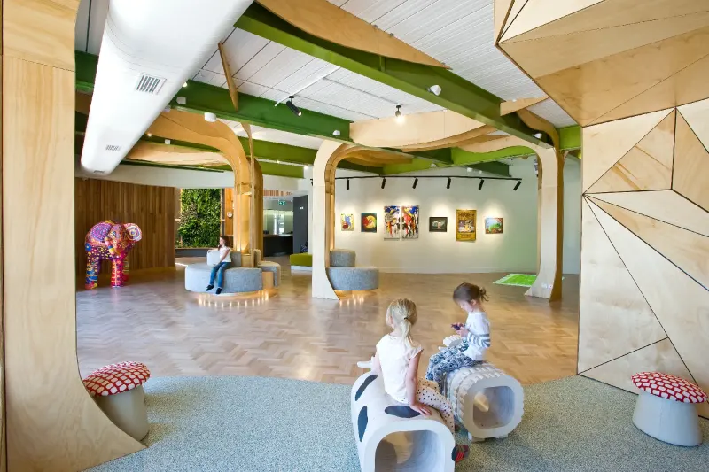 Early learning centre interior with timber tree columns, green ceiling beams and children playing