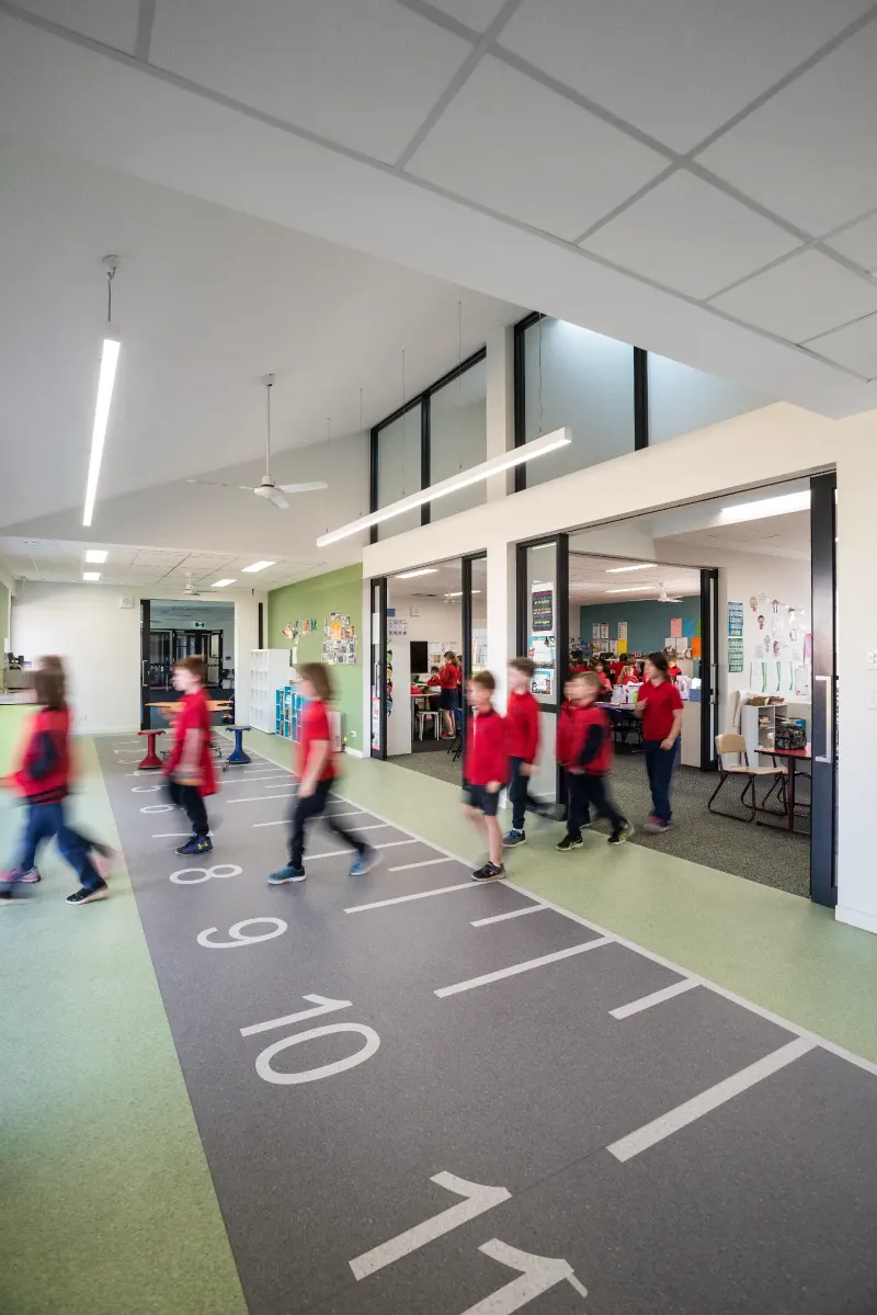 Primary school corridor with a running-track floor graphic and children moving between classrooms