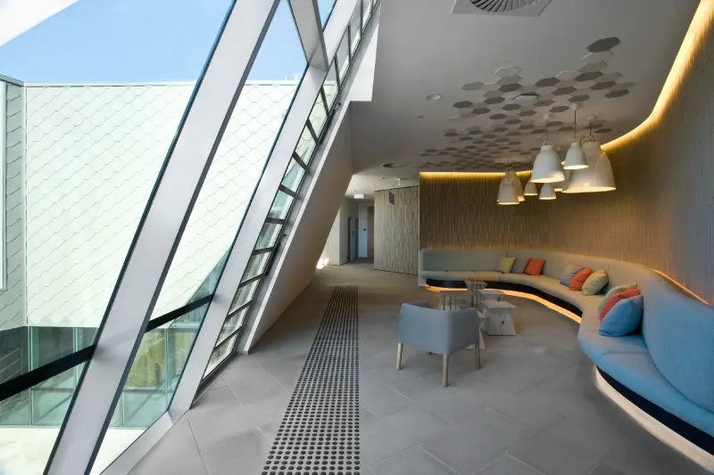 Lobby seating area beneath raking glazing with a curved built-in sofa and pendant lights
