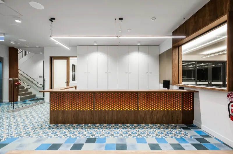 Reception desk with perforated timber front and patterned encaustic tile flooring