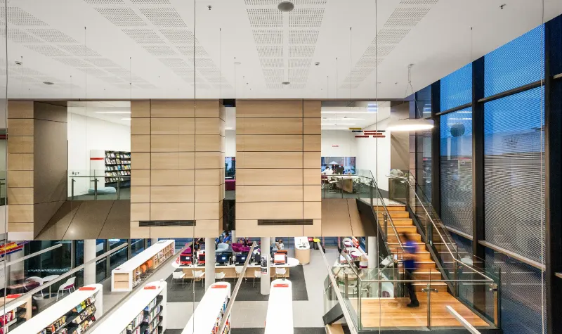 Library interior viewed from the mezzanine, timber-clad volumes above open stacks