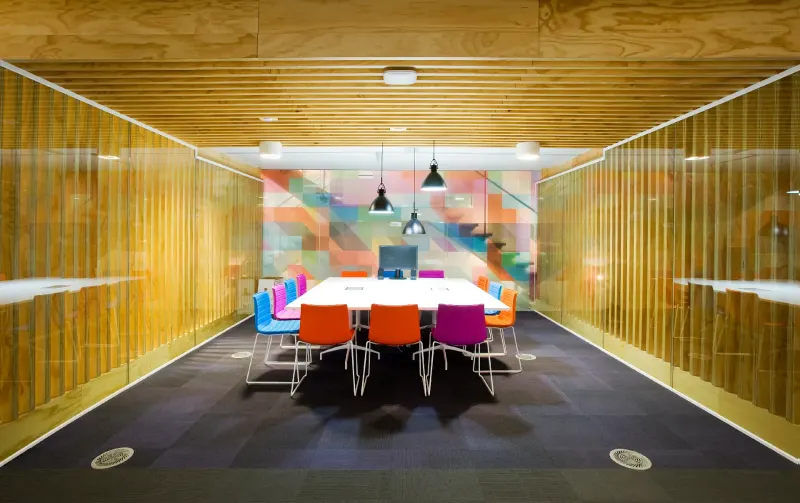 Meeting room enclosed in gold mesh screens with a colourful mural and orange chairs
