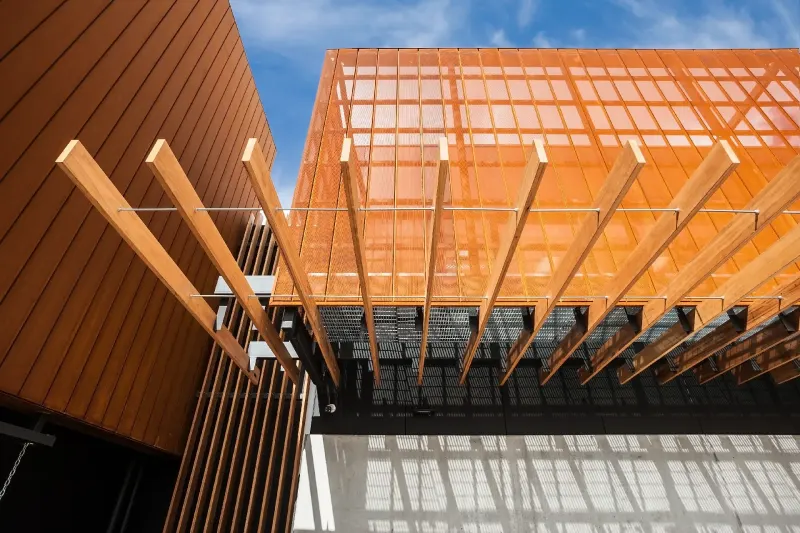 Detail of an orange timber brise-soleil and batten screen against a blue sky