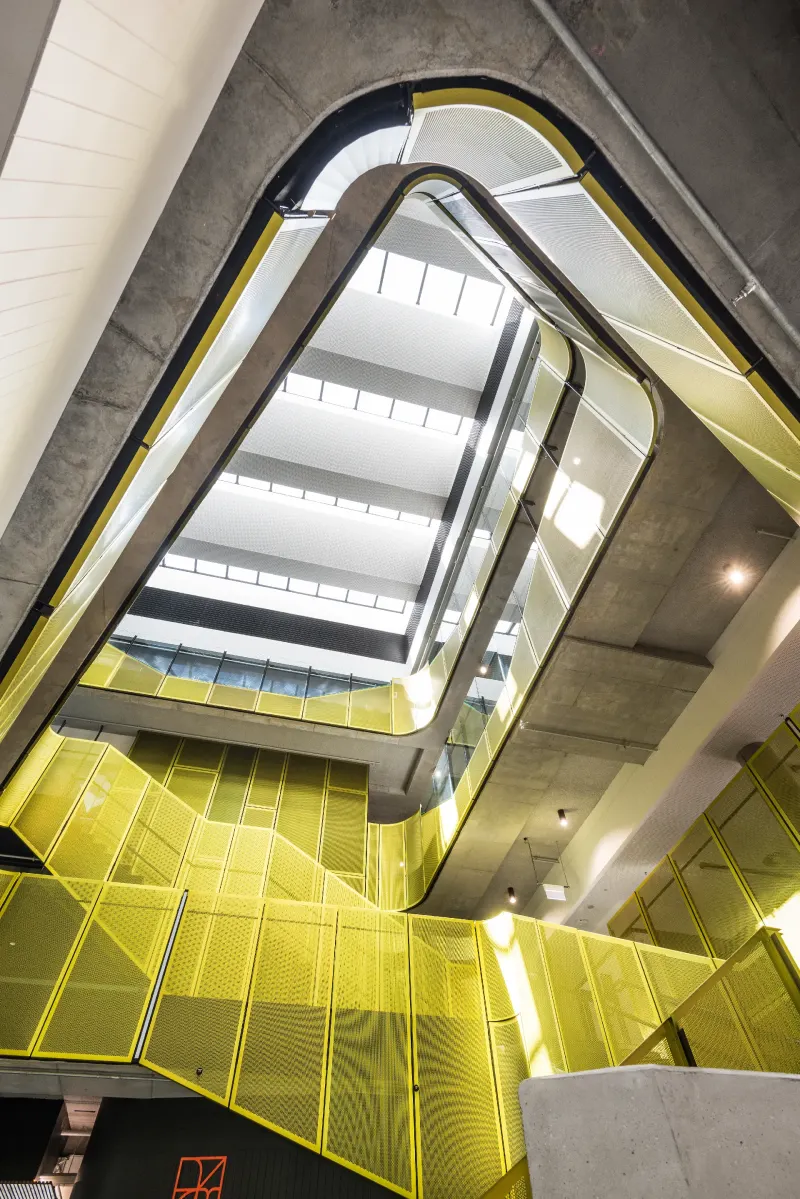Yellow perforated metal balustrades winding through a raw concrete atrium stairwell