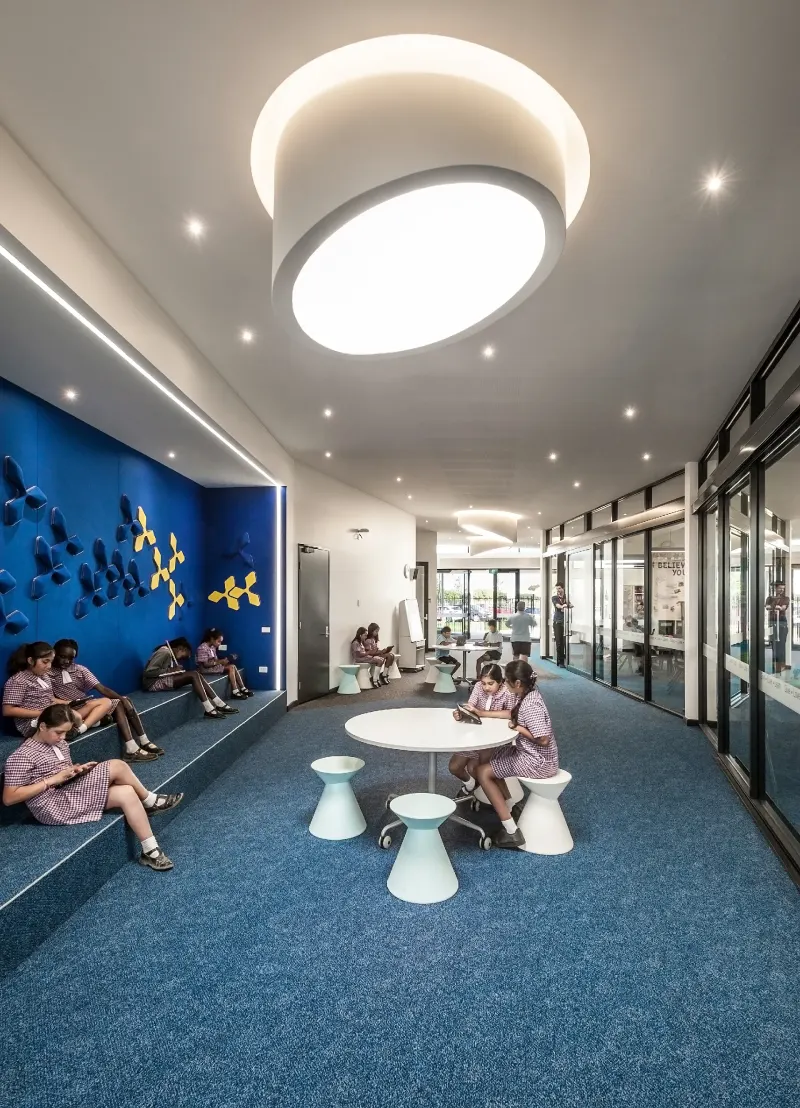 School breakout space with tiered blue seating, students reading and a circular skylight fitting