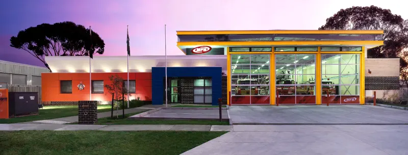 Colourful single-storey community hub photographed at dusk with warm interior light