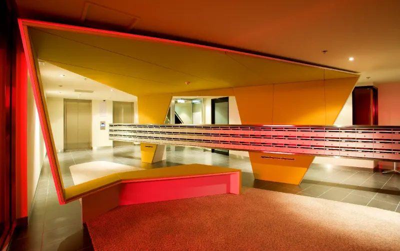 Angular foyer in red and ochre with a cantilevered bench and folded ceiling planes