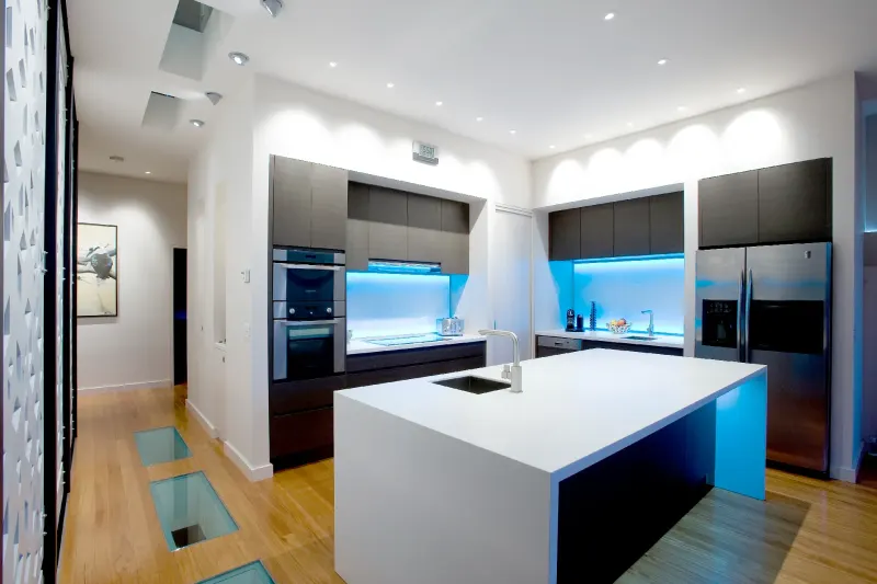 Minimalist residential kitchen with a white stone island bench and backlit glass splashback